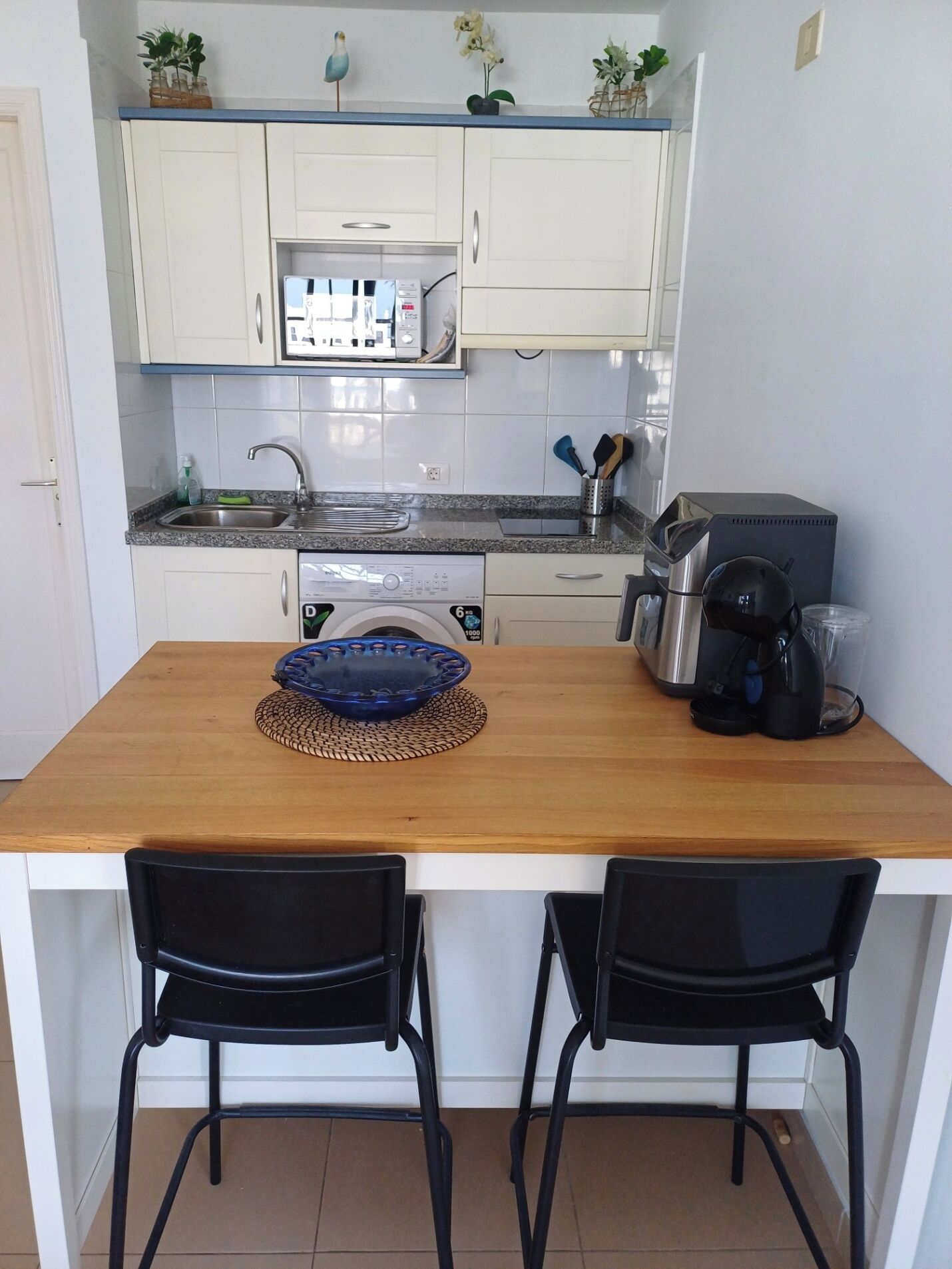 A compact kitchen with white cabinets, a microwave, a coffee maker, and two black chairs.