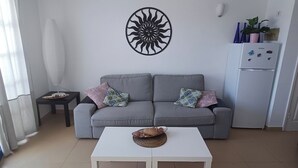 Un salón con un sofá gris, una mesa de centro blanca y un adorno en la pared.