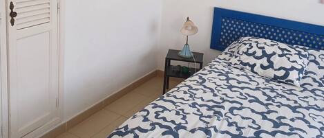 Een slaapkamer met een bed, nachtkastje, lamp, garderobe en een blauw hoofdeinde.
