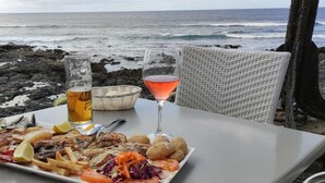 Una mesa con mariscos, bebidas y pan junto al mar.