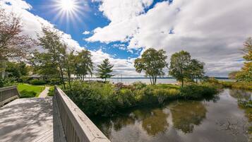 A wooden deck overlooking a calm lake with trees and a clear sky.