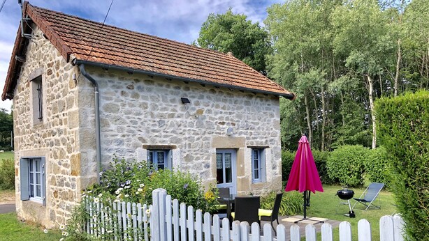 A stone house with a tiled roof, a white picket fence, and a pink umbrella. - House made of regional stones, typical from Auvergne, greenery landscape (Gouttières)