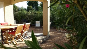 A covered patio with a wooden table and chairs, surrounded by greenery and a gravel path. - Modern mini villa T3 800 m from the beach - all comforts, air conditioning, terrace (Lecci)