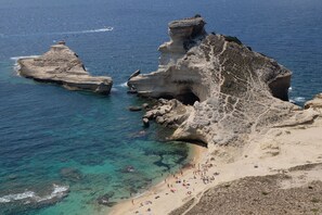 Una spiaggia costiera con acque limpide, formazioni rocciose e un lido sabbioso.