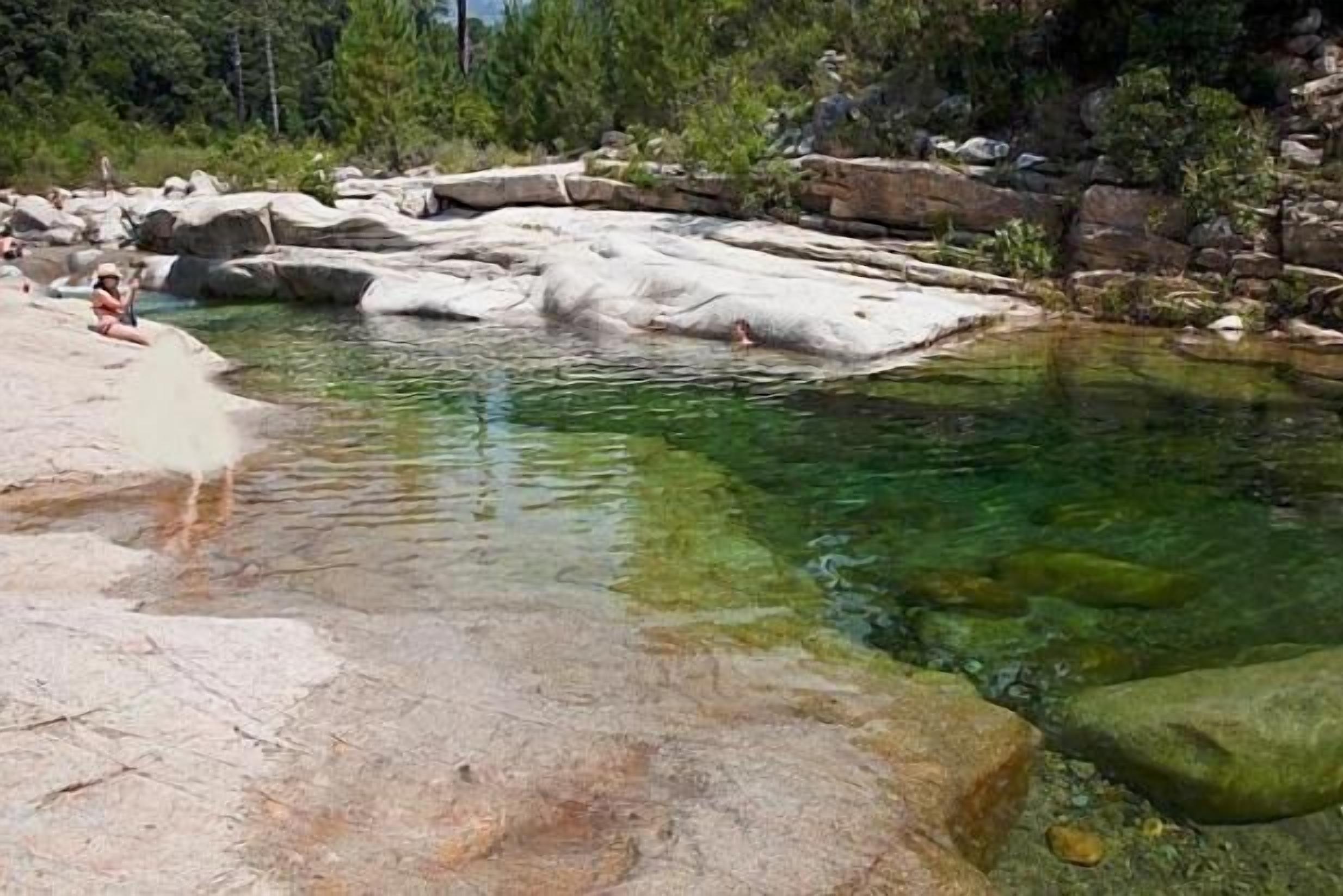 A natural pool surrounded by large rocks and trees.