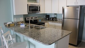 A kitchen with granite countertops, stainless steel appliances, white cabinets, and a small dining area with white chairs. - Perfect Family or Romantic Getaway~Best View in Orange Beach~Summer specials (Orange Beach)