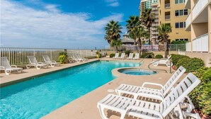 A pool area with lounge chairs and a hot tub, surrounded by palm trees and a building with balconies. - Perfect Family or Romantic Getaway~Best View in Orange Beach~Summer specials (Orange Beach)