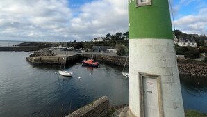 A lighthouse with a green and white exterior, situated by a calm harbor with boats docked nearby.
