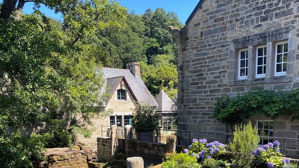A stone building with a traditional design, a small bridge over a water feature, and lush greenery.
