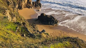 A coastal landscape with rocky cliffs, a sandy beach, and a clear sky.