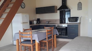 Cocina compacta con refrigerador, microondas y estufa. Cuenta con una mesa de comedor con sillas y una cama en la habitación.