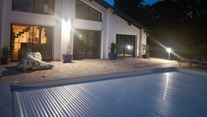 Ein modernes, zweistöckiges Haus mit Pool, großen Fenstern und Kübelpflanzen.