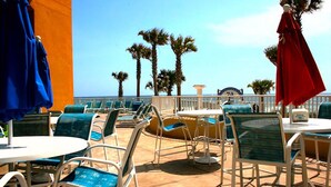 A beachside patio with outdoor seating, palm trees, and a view of the ocean.