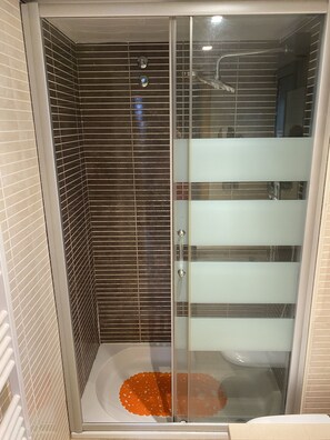A glass-enclosed shower stall with a tiled wall and a white floor. - Panoramic view of the Mediterrannée, apartment on canal near beach  (Rosas)