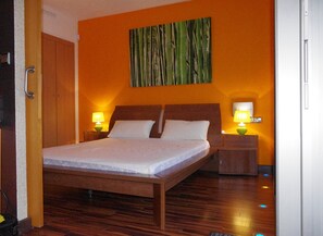 A hotel room with a wooden bed, two bedside lamps, a wall-mounted painting, and a wooden wardrobe. - Panoramic view of the Mediterrannée, apartment on canal near beach  (Rosas)