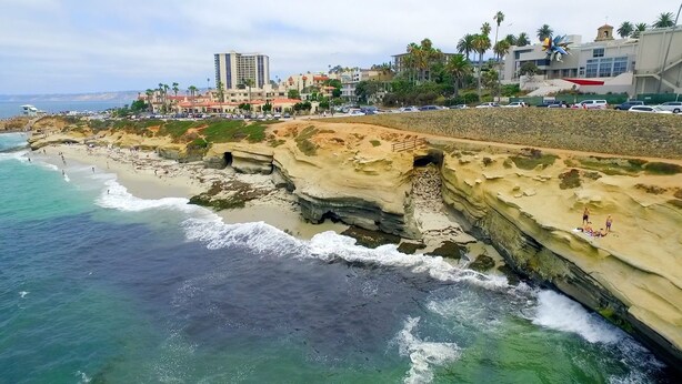 A coastal hotel with a rocky shoreline, ocean waves, and a view of the cityscape in the background. - “Blue Door Cottage by the Sea,” La Jolla Village & Cove, Only 4 blocks to Beach  (La Jolla)