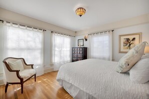 Quarto com uma cama grande, uma cadeira de madeira e uma mesa de cabeceira com abajur.