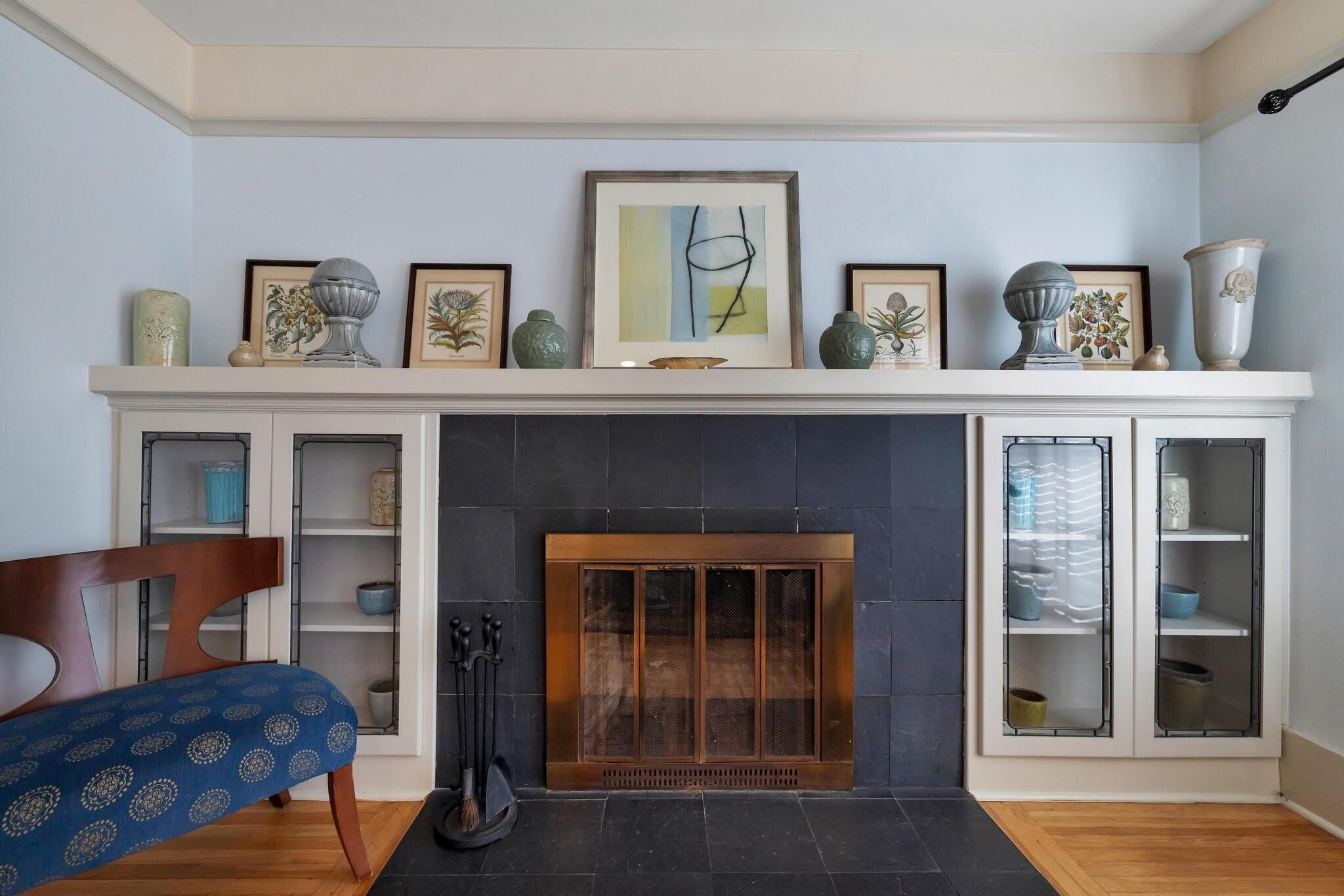 A living room with a fireplace, a blue patterned sofa, and a mantel decorated with framed artwork and vases.