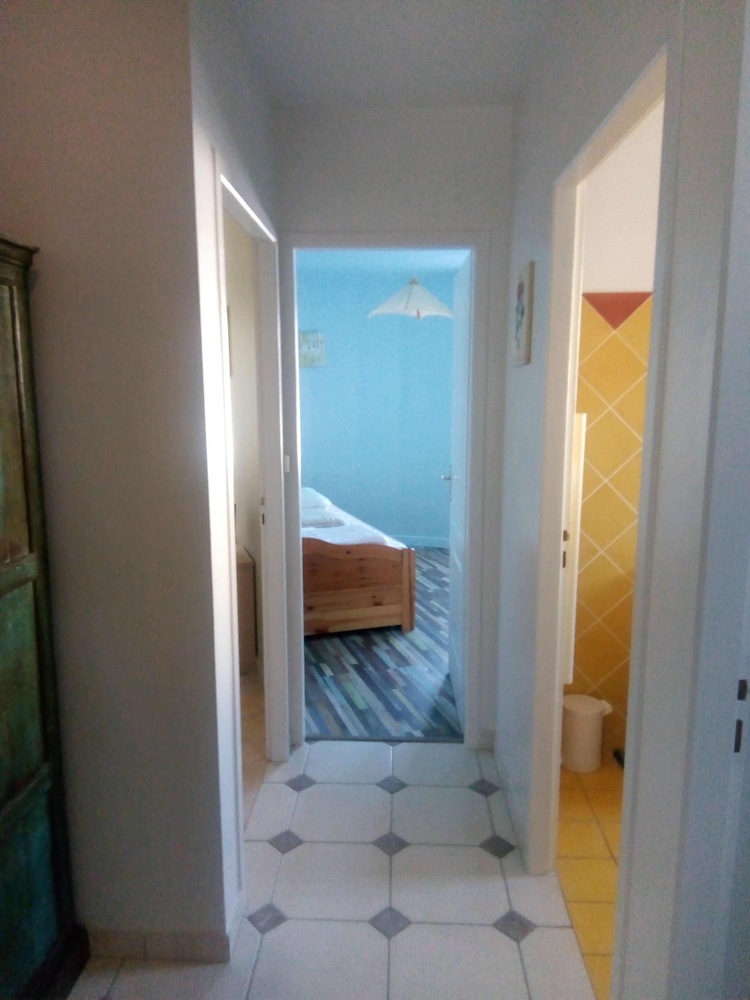 A narrow hallway with a bed in the background, a tiled floor, and a door on the right.