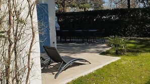 Ein moderner Außenbereich zum Sitzen mit einem Metallstuhl und einem Tisch, umgeben von einem gepflegten Rasen und einer Hecke.