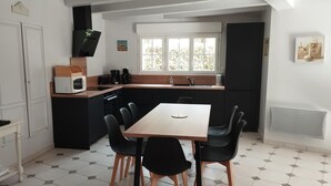 Eine kompakte Küche mit Essbereich, ausgestattet mit einem Holztisch, schwarzen Stühlen, einer Mikrowelle und einer Kaffeemaschine.