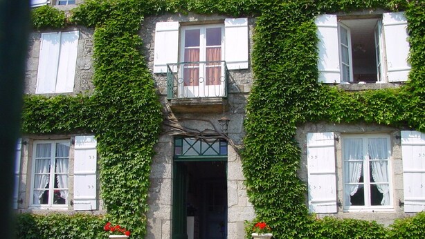 Un edificio de piedra con entrada verde, contraventanas blancas y un pequeño balcón.