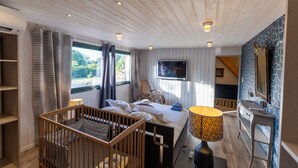 Una habitación con una cuna, una cama, un televisor, un escritorio y un espejo.