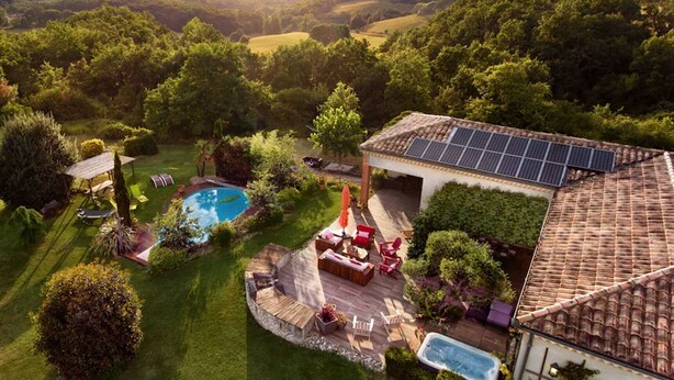 Propiedad residencial con piscina, zona de estar exterior y paneles solares en el techo.