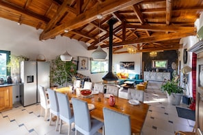 Een ruime keuken met moderne apparatuur, een eethoek met een houten tafel en stoelen, en een gezellige woonkamer met een bank en open haard.