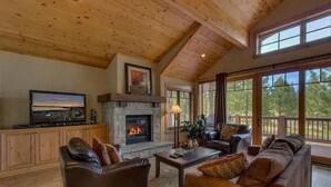 A spacious living room with a fireplace, leather sofas, a television, and large windows offering a view of the outdoors. - "Lovely Lookout" Ski, Golf & Club Amenities Schaffer's Mill, Lake Tahoe (Truckee)