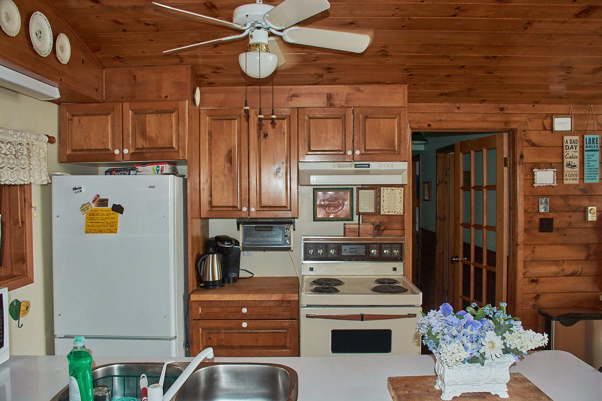 A kitchen with wooden cabinets, a refrigerator, a stove, and a ceiling fan.