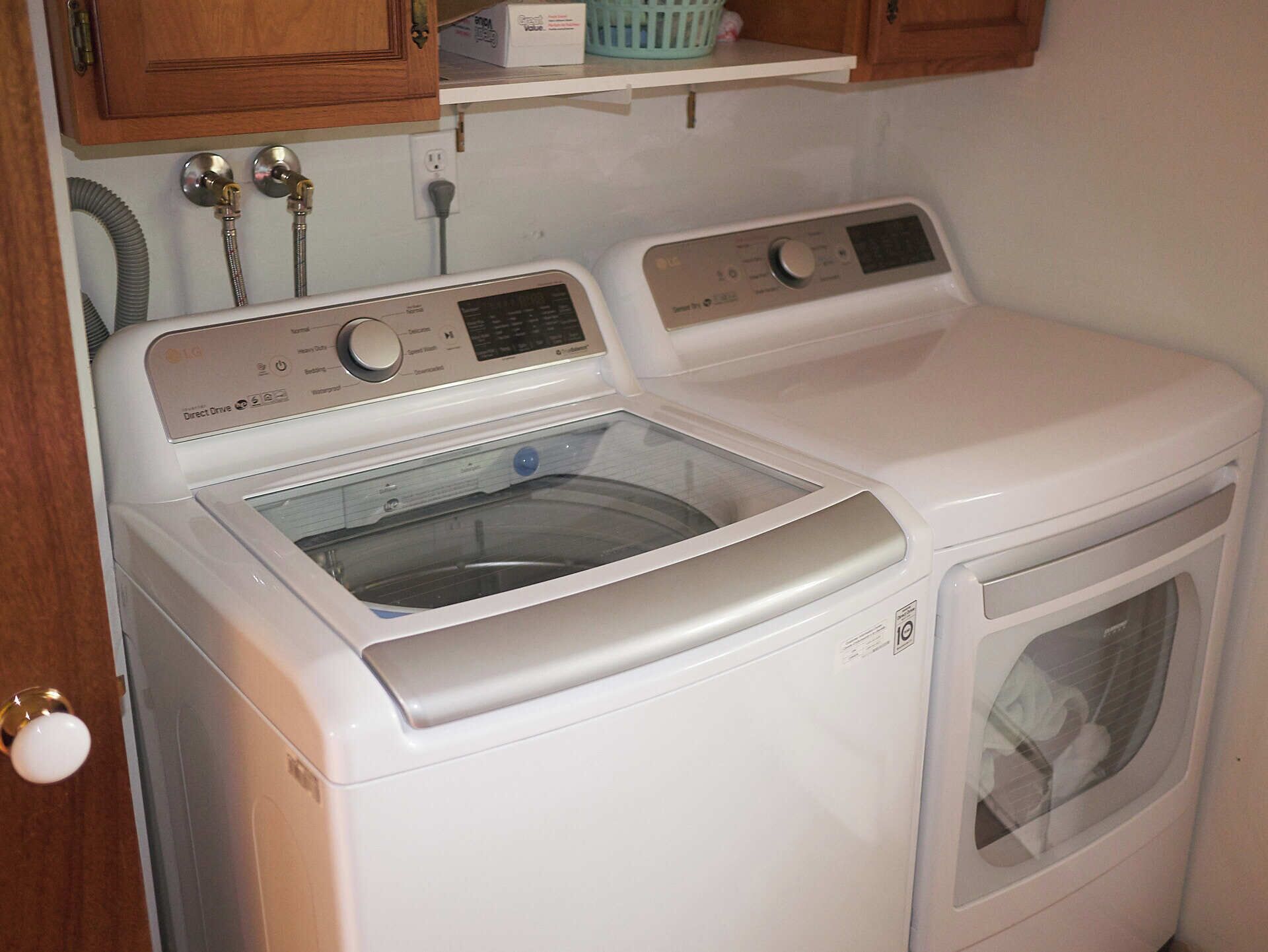 Un appareil combiné lave-linge et sèche-linge à chargement frontal, doté d’un panneau de commande, d’une étiquette indiquant qu’il est à entraînement direct et d’un tuyau d’arrivée d’eau.