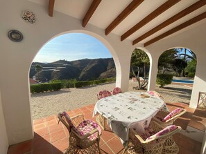 An outdoor patio with a round table and wicker chairs, overlooking a scenic landscape with hills and a clear sky. - Independent villa, magnificent sea view, private swimming pool, WIFI (ALGARROBO)