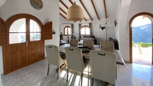 A spacious dining area with a round table and six chairs, wooden beams on the ceiling, and large arched windows. - Independent villa, magnificent sea view, private swimming pool, WIFI (ALGARROBO)