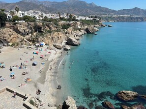 Una spiaggia costiera con acque cristalline, terreno roccioso e una cittadina sullo sfondo.