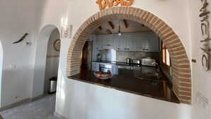 A kitchen with an arched brick feature, white cabinets, and a countertop with a bowl of fruit.