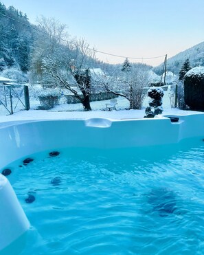 A hot tub in a snowy outdoor setting with a view of snow-covered trees and hills.
