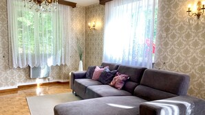 Een woonkamer met een grijze bank, witte gordijnen en een kroonluchter.