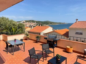 A terrace with a table and chairs, a grill, and a view of the sea and town. - LUXURY SEA AND MOUNTAIN APARTMENT (Banyuls-Sur-Mer)