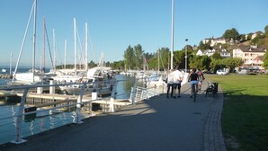 Un puerto deportivo con barcos amarrados, un sendero junto al agua y casas al fondo.
