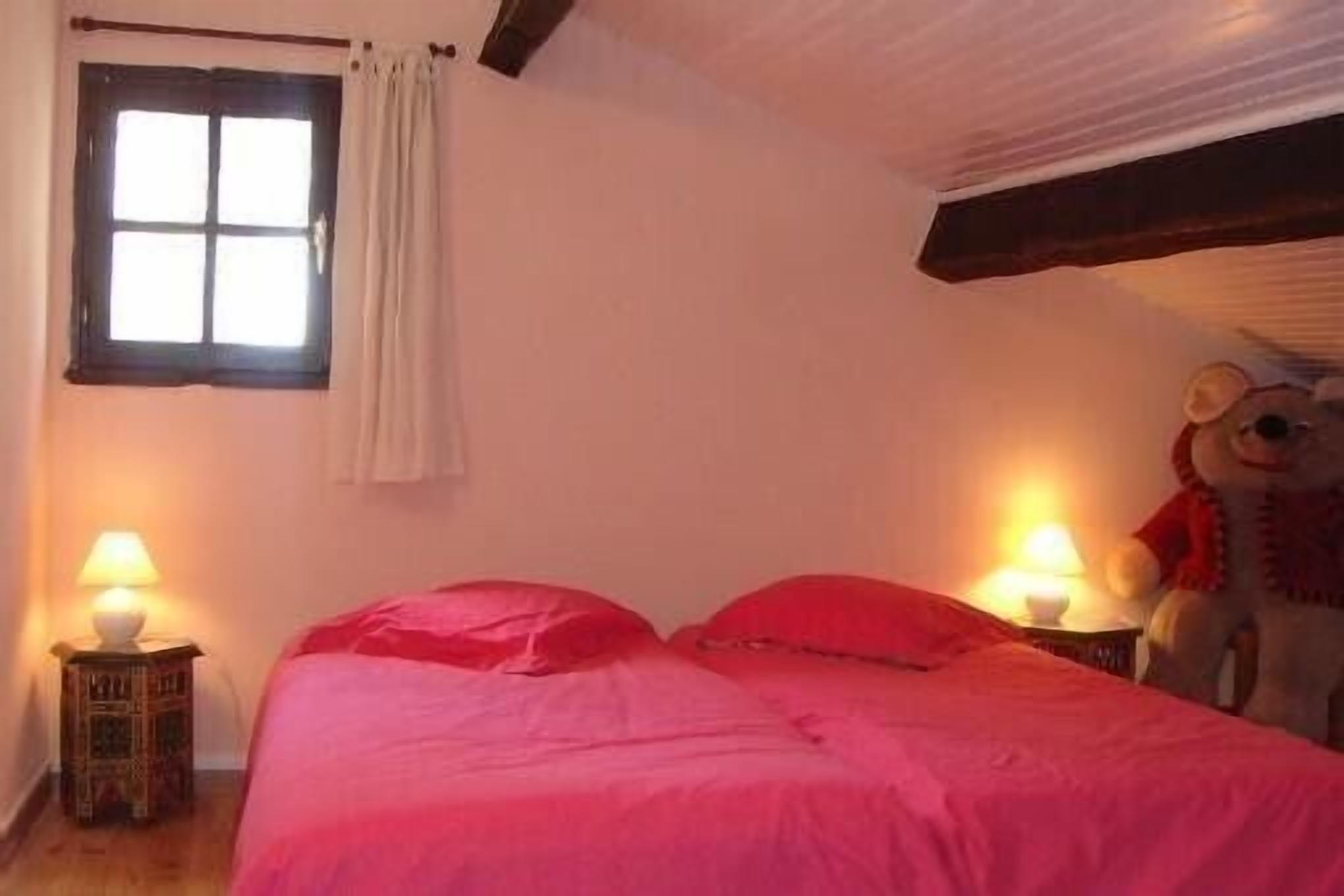 Une chambre à coucher avec un lit, deux lampes de chevet, une fenêtre avec des rideaux et un ours en peluche sur le côté droit.
