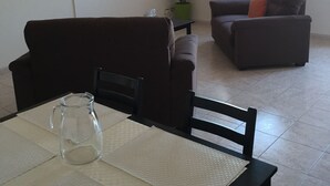 A living room with a TV mounted on the wall, a dining table with a pitcher, and a sofa with cushions. - Cefalù Appart 4 (Cefalù)