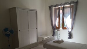 A bedroom with two beds, a wardrobe, a radiator, a fan, and a window with curtains. - Cefalù Appart 4 (Cefalù)