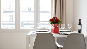 A dining table set with a vase of red flowers, wine glasses, and a bottle of wine.