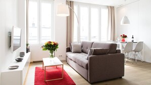 A modern living room with a grey sofa, a red rug, a white coffee table, and a TV on a white stand.