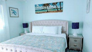 Une chambre avec un lit, deux tables de chevet, un hamac suspendu et un tableau sur le thème de la plage.