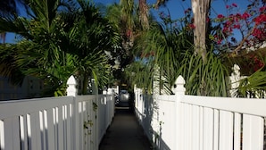 Un sentier bordé de clôtures blanches et d’une végétation luxuriante, qui mène à un bâtiment.