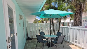 Une terrasse avec une table et des chaises, une clôture blanche et un palmier.