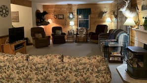 Ein gemütliches Blockhaus-Interieur mit Holzwänden, Kamin, Fernseher und verschiedenen Jagdtrophäen.