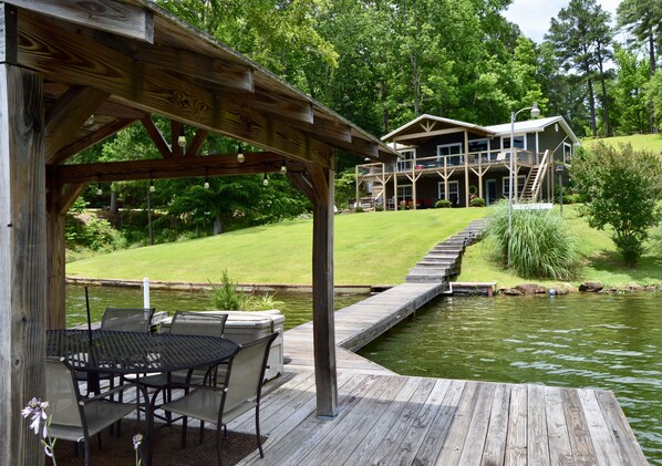 A wooden deck with a table and chairs, a pond, and a house in the background. - Spring special! Enjoy Lake Martin at its best! (Jacksons Gap)